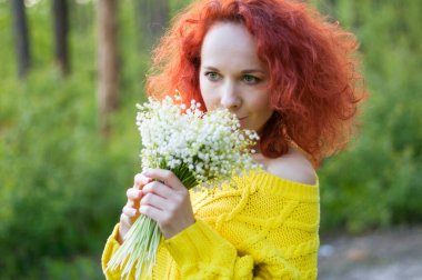 Kızıl saçlı, kıvırcık saçlı, sarı kazaklı, beyaz çiçeklerle poz veren güzel bir kız.