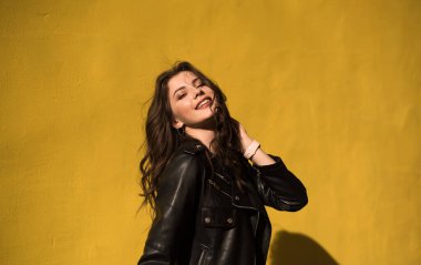 Parlak turuncu arka planda deri ceketli, esmer, kaygısız, güzel bir kız. Genç mutlu kadın güneşli bir günde şehirde