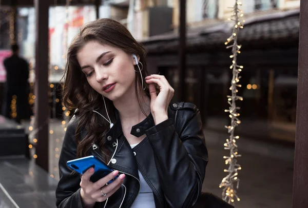 pretty white student girl listens romantic music in an earphones in city