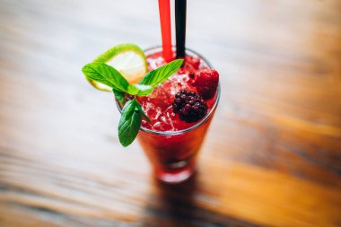 Pembe, taze, nefis bir kokteyl. Nane pipetleri ve gece kulübü barında kırmızı böğürtlenler. Bu, pencerenin önündeki ahşap masaya seçici odaklı kokteyl bardağı.
