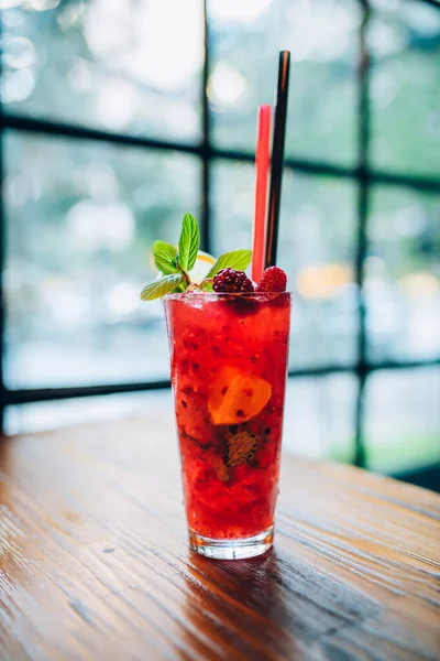 Pembe, taze, nefis bir kokteyl. Nane pipetleri ve gece kulübü barında kırmızı böğürtlenler. Bu, pencerenin önündeki ahşap masaya seçici odaklı kokteyl bardağı.
