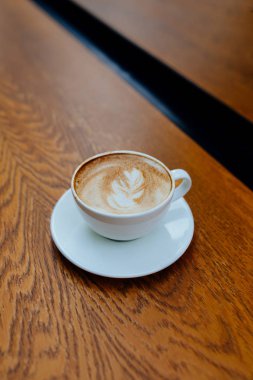 Ahşap masa arkasında bir fincan kahve. Güzel latte sanatı.