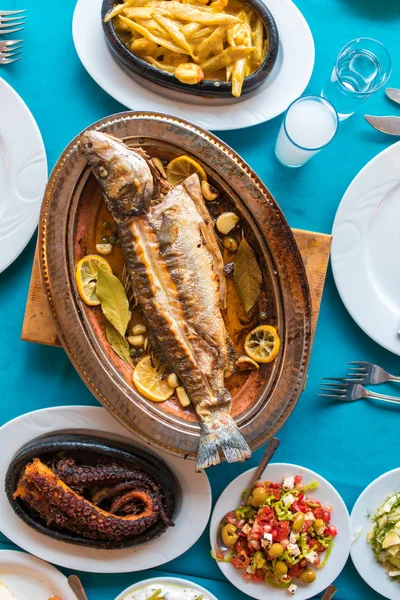 Turkish or Greek restaurant table and food dinner cuisine culture from top view. Traditional Greek ouzo or turkish raki with grilled or fried fish and appetizers on dinner table at restaurant. Fish restaurant in Turkey or Greece