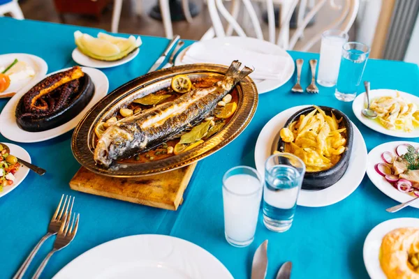 Turkish or Greek restaurant table and food dinner cuisine culture from top view. Traditional Greek ouzo or turkish raki with grilled or fried fish and appetizers on dinner table at restaurant. Fish restaurant in Turkey or Greece