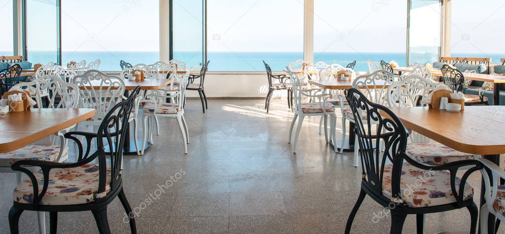 View of restaurant or cafe on beach in Gumusluk, Bodrum city of Turkey. Aegean seaside style colorful chairs, tables and flowers in Bodrum town near beautiful Aegean Sea.