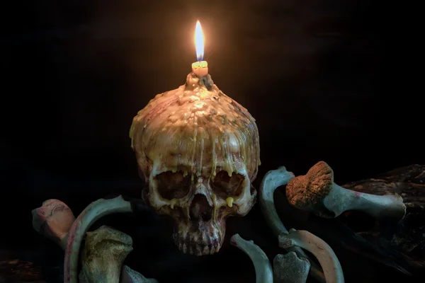 Crânio com luz de vela em cima e osso em madeira grunge em preto — Fotografia de Stock