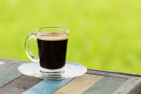 Café preto quente na mesa de madeira com fundo de natureza verde — Fotografia de Stock