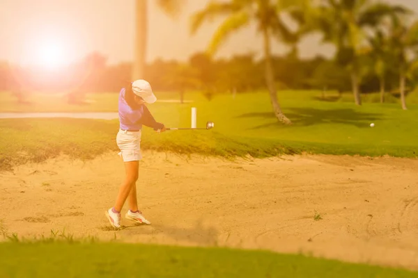 Gracz w golfa kobiet swinging golf z piasku bunkier podczas zachodu słońca — Zdjęcie stockowe