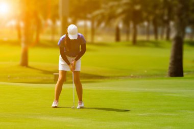 Golf ile flar günbatımı sırasında yeşil koyarak kadın golf oyuncu