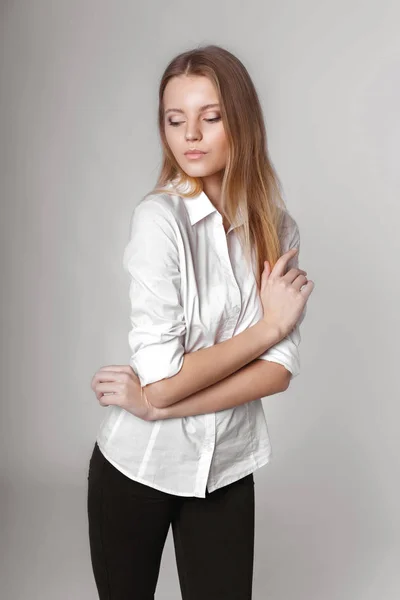 Retrato de moda de una chica posando en un estudio amplio y luminoso con un fondo gris en una ropa cómoda y sencilla con estilo. chica joven con la piel limpia y la cara perfecta — Foto de Stock