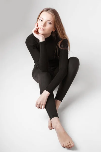 Retrato de moda de uma menina posando em estúdio brilhante e espaçoso com um fundo cinza em uma roupa elegante confortável e simples. jovem com pele limpa e rosto perfeito Imagem De Stock