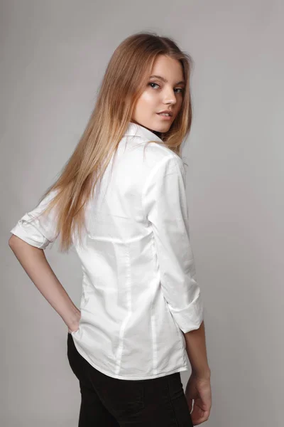 Retrato de moda de una chica posando en un estudio amplio y luminoso con un fondo gris en una ropa cómoda y sencilla con estilo. chica joven con la piel limpia y la cara perfecta —  Fotos de Stock