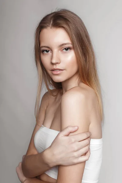 Retrato de moda de una chica posando en un estudio amplio y luminoso con un fondo gris en una ropa cómoda y sencilla con estilo. chica joven con la piel limpia y la cara perfecta Imagen de stock