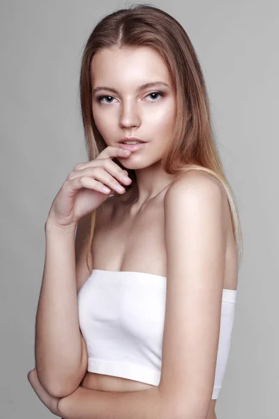 Retrato de moda de una chica posando en un estudio amplio y luminoso con un fondo gris en una ropa cómoda y sencilla con estilo. chica joven con la piel limpia y la cara perfecta Imagen de archivo