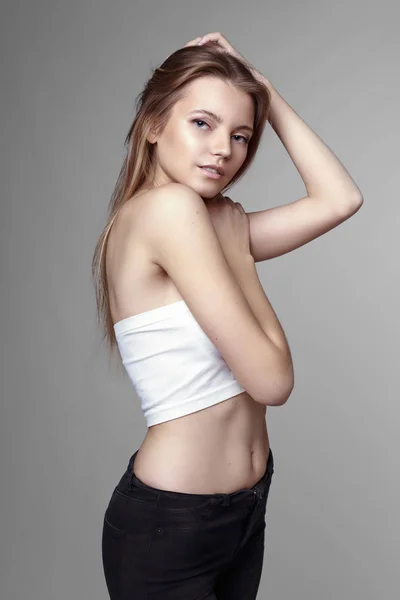 Retrato de moda de una chica posando en un estudio amplio y luminoso con un fondo gris en una ropa cómoda y sencilla con estilo. chica joven con la piel limpia y la cara perfecta Fotos de stock libres de derechos