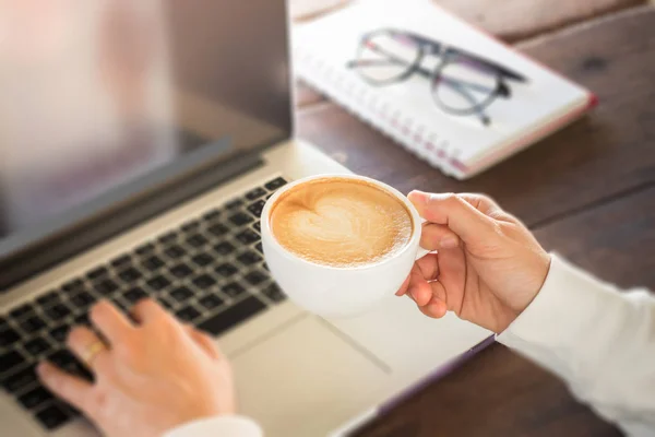 Hand on cup of coffee at work table — Stock Photo, Image