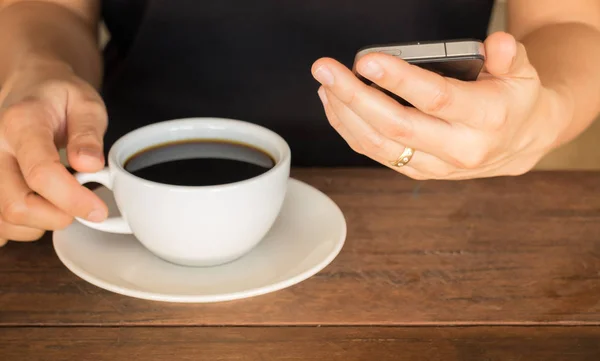 Hand on coffee cup and smartphone — Stock Photo, Image