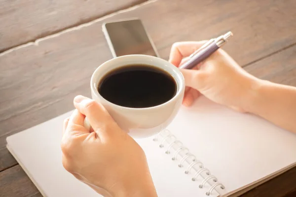 Ręka na filiżankę kawy i pisania — Zdjęcie stockowe