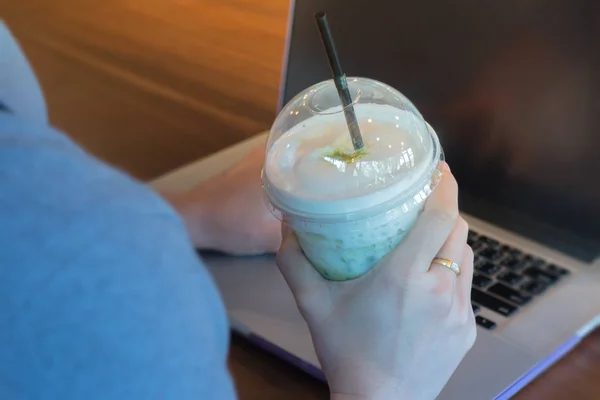 Vrouw Hand op Iced melk groene thee tijdens het typen — Stockfoto