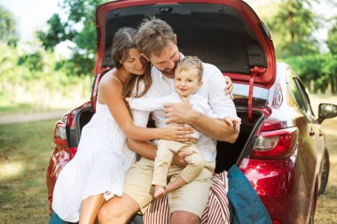 Genç bir aile. Beyaz elbiseli üç kişi piknik yapıyor. Güzel ebeveynler ve oğullar yaz tatilinde arabayla seyahat ederler. Parkta Sahne