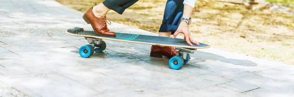 Businessman person in brown leather boots is riding on skateboard in park. Concept of escape from office and got freedom. Hobby as way to relax. Banner
