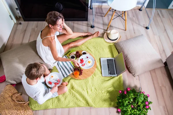 Happy mom and boy imitating summer picnic time with father near lap top blanket .Travelling with family. Coronavirus situation in tourism industry. Quarantine. Stay at home online. Isolation. Top view