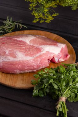Tahtada büyük bir parça et var. Siyah arka plan, maydanoz. Yemek tarifi için fotoğraf. Dikey