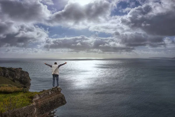 Молодий чоловік на краю скелі, хмарно і похмурий морський пейзаж — стокове фото