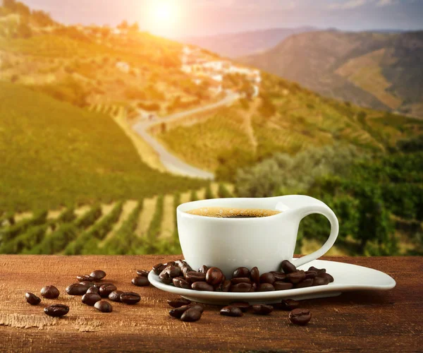 Xícara de café com grãos de café na mesa de madeira e plantações — Fotografia de Stock
