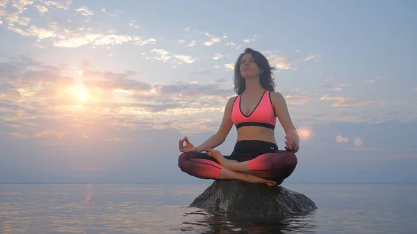 Mujer yoga en pose de loto sobre roca en agua de mar — Foto de Stock