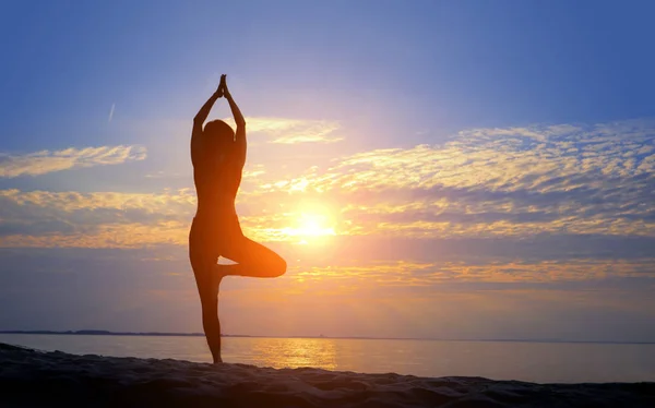 Silueta femenina haciendo yoga asana al amanecer con las manos levantadas al sol — Foto de Stock