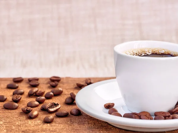 Xícara de café e pires em uma mesa de madeira com grãos — Fotografia de Stock