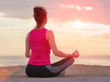 Tahta iskelede yoga yapan güzel bir kadın. Deniz ve gün batımı gökyüzü arkaplanı.