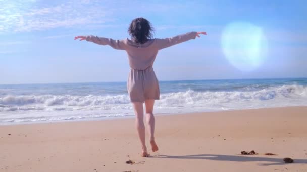Kvinna promenader med armarna upp på stranden, lins blossa effekter — Stockvideo