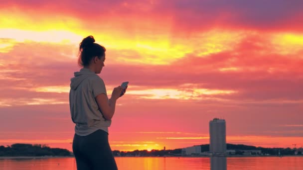 Donna caucasica in abiti sportivi con smartphone al tramonto, Travemunde, Germania — Video Stock