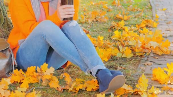 Mulher no parque de outono, beber café e desfrutar do sol de outono — Vídeo de Stock