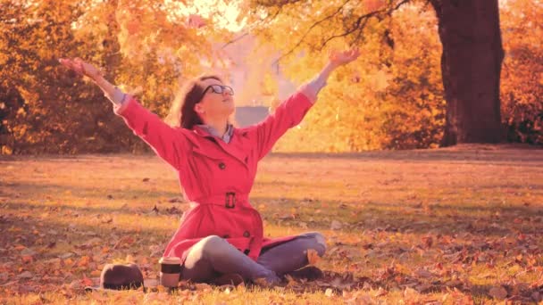 Жінка в червоному плащі кидає осіннє листя в парку — стокове відео