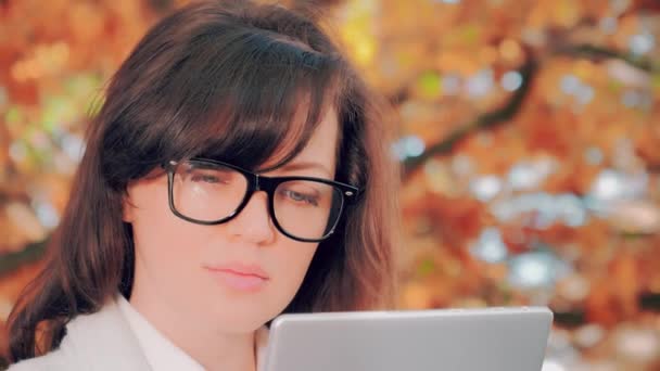 Νεαρή γυναίκα στο πάρκο το φθινόπωρο εργάζεται με το tablet της — Αρχείο Βίντεο