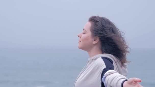 Retrato de uma mulher de olhos azuis na praia desfrutando de um dia chuvoso cinza . — Vídeo de Stock