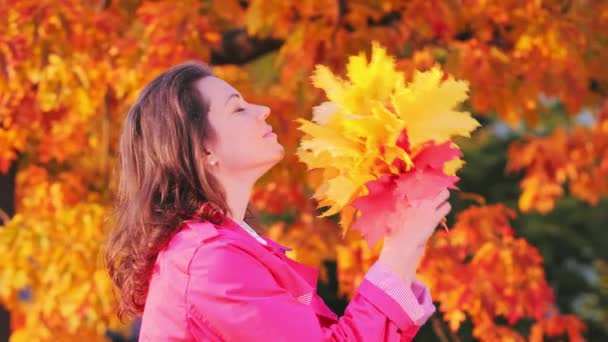 Молодая женщина с букетом желтых осенних листьев, наслаждается осенним временем — стоковое видео