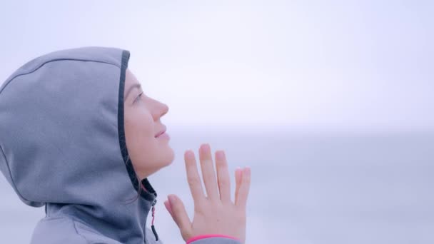 Mujer rezando en impermeable bajo la lluvia en la playa nublada gris — Vídeos de Stock