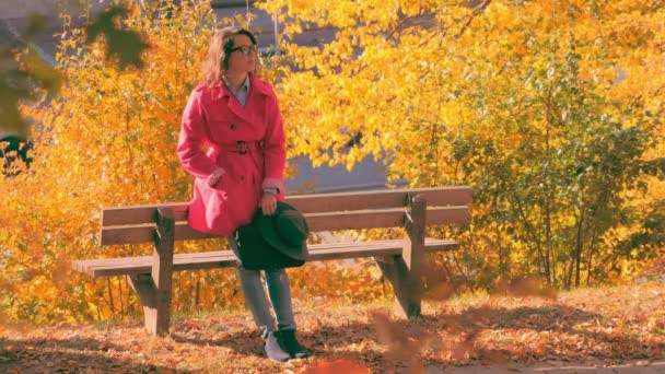 Жінка розмовляє по смартфону і чекає когось в парку — стокове відео