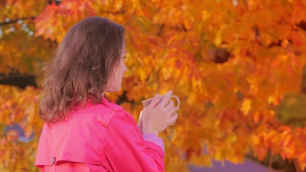 Жінка п'є гарячий напій в осінньому саду — стокове відео