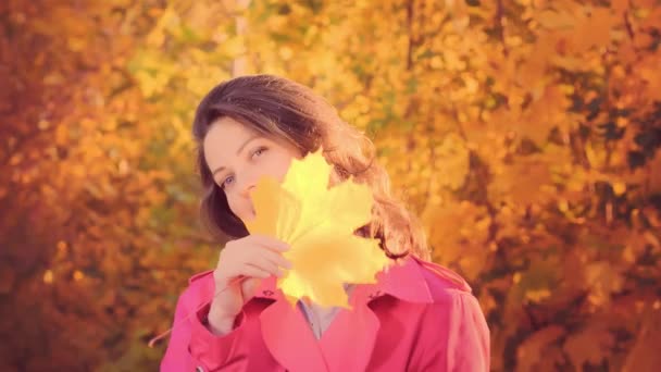 Молодая женщина с желтым осенним листом, осеннее время — стоковое видео