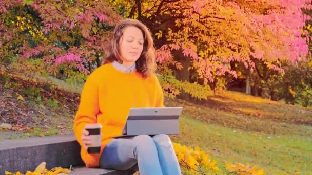 Красива жінка працює з ноутбуком і насолоджується осінь в парку — стокове відео