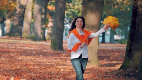 Young woman with a bouquet of yellow autumn leaves in park, enjoying leaf fall — 비디오