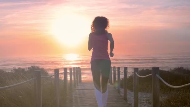 Rennende vrouw in fitnesskleding aan de oceaan. Vrouw loopt langs houten loopbrug — Stockvideo