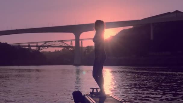 Молодая танцовщица на берегу реки на закате — стоковое видео