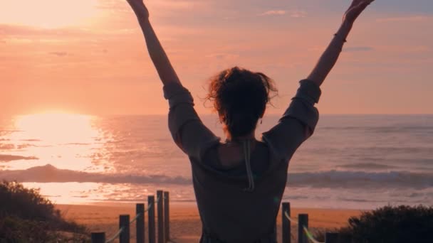 Mujer caminando con los brazos en el puente de madera en la playa al atardecer — Vídeos de Stock