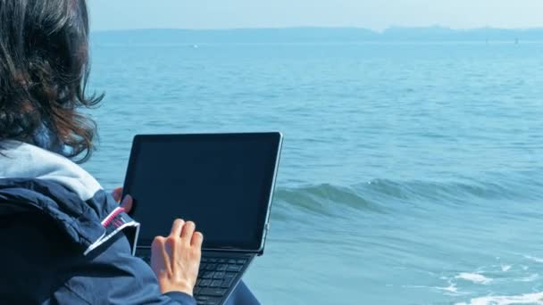 Frilansande livsstil, kvinna som sitter på havskusten och använder laptop. — Stockvideo